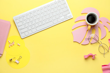 Computer keyboard with cup of coffee, eyeglasses and stationery on color background
