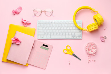 Computer keyboard with stationery, headphones and eyeglasses on color background