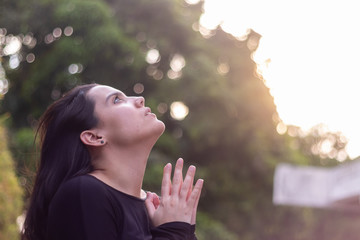 Young woman in a garden, gestures with her hands to pray, while looking up