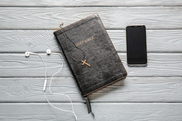 Holy Bible, mobile phone and earphones on wooden background