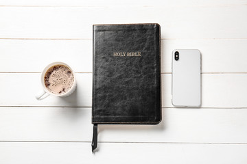 Holy Bible, cup of coffee and mobile phone on white wooden background