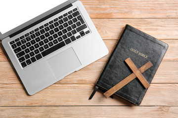Holy Bible, laptop and cross on wooden background