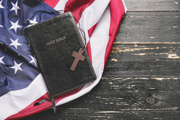Holy Bible, cross and USA flag on wooden background