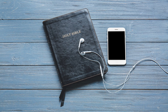Holy Bible, mobile phone and earphones on wooden background