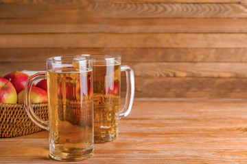 Mugs of apple cider on wooden background