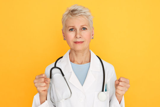Stay strong. Portrait of serious senior female physician in medical uniform clenching fists, encouraging patients to figth against disease, her look full of hope and determination. Medicare and health
