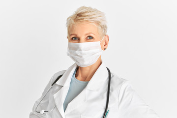 People, lifestyle, job and medical occupation concept. Portrait of serious blonde middle aged female doctor wearing white surgical mask to protect herself from contagious disease during pandemic