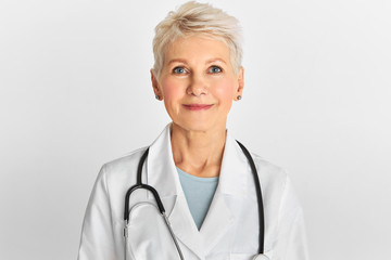 Studio image of confident attractive middle aged female doctor with short dyed hairstyle posing...