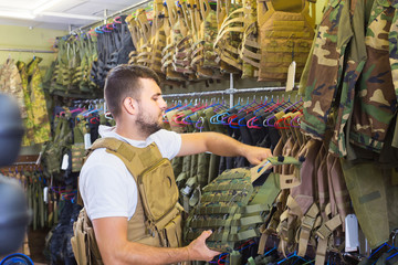 Obraz na płótnie Canvas Young guy choosing flak jacket in military shop