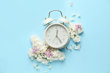 Composition with beautiful lilac flowers and alarm clock on color background