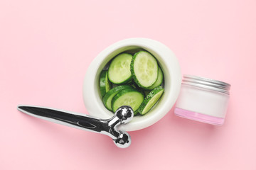 Cucumber, cream and massage tool on color background