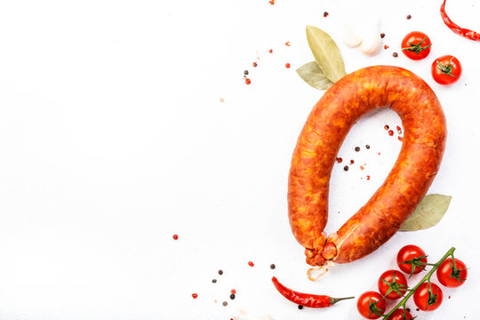 Smoked sausage on white kitchen table background with aromatic herbs and spices, tomatoes and garlic, natural organic farm meat product, top view, copy space