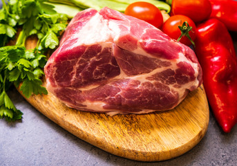 Pork meat on a cutting board surrounded by vegetables