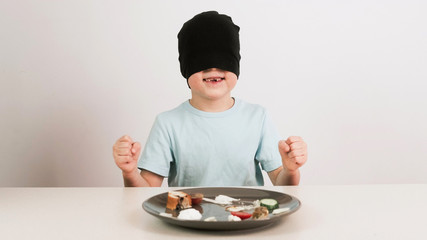 A boy in a black mask tries and guesses a variety of foods