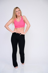 A slender Caucasian model poses in various poses with a smile. Portrait of a pretty fitness blonde girl in a sports uniform on a white background in full growth.