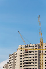 Construction site. Unfinished apartment buildings. Construction workers laying bricks on top. Special industrial cranes in the middle. Blue sky background.