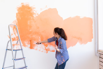 Happy smiling woman painting interior wall of new house. Redecoration, renovation, apartment repair and refreshment concept.