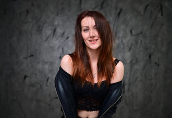 Fototapeta premium Studio portrait of a caucasian young brunette woman with minimal makeup. A pretty model is standing on a gray background in a black jacket.