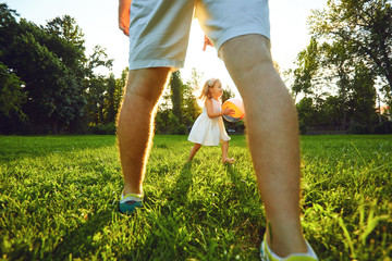 Father plays with his daughter on a tarve ball in a park at sunset.
