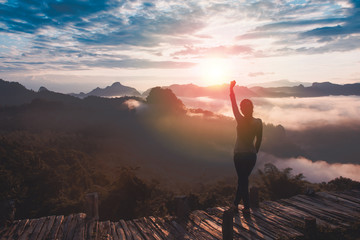 Happy celebrating winning success woman at sunrise standing elated with arms raised up above her head in nature, Lifestyle freedom concept adventure active vacations  over clouds harmony with nature