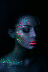 Fashion model woman in neon light bright fluorescent makeup, drop on face. Beautiful model brunette...