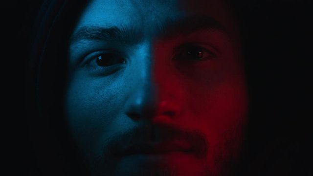 Portrait of Young Serious Man on Black Background. Face Expression in Colour Filter of Trendy Neon Uv Light. Young Man Looking at Camera Close Up Indoors. 4k Footage.