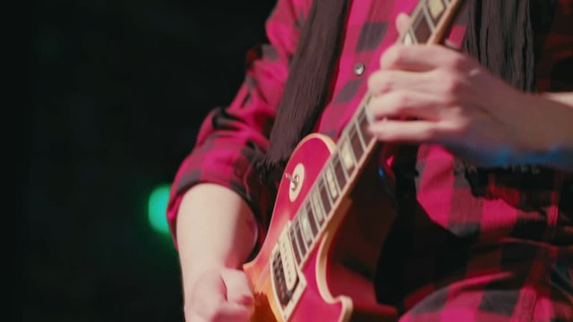 Detail shot of a man in a red shirt enthusiastically playing his e-guitar at a concert.