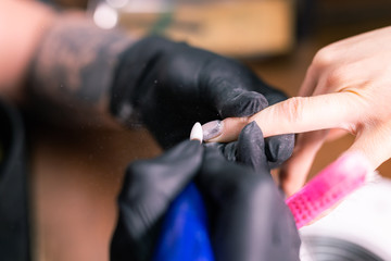 Naklejka premium Female master uses an electric machine to remove the nail polish during manicure in the salon. Close-up hardware manicure. Concept of hand care. Female manicurist cleaning of nails by a milling cutter