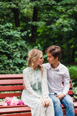 A girl and a man walk in the park in the summer, chatting, joy, love, relationships, bench and trees, family, meeting and flirting, peonies, flowers