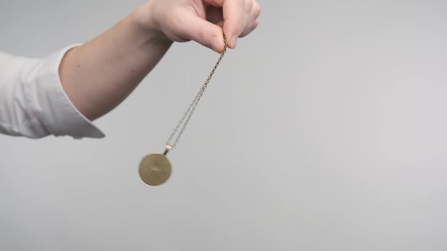 hypnosis session pendant on chain sways in female hand of hypnotist.