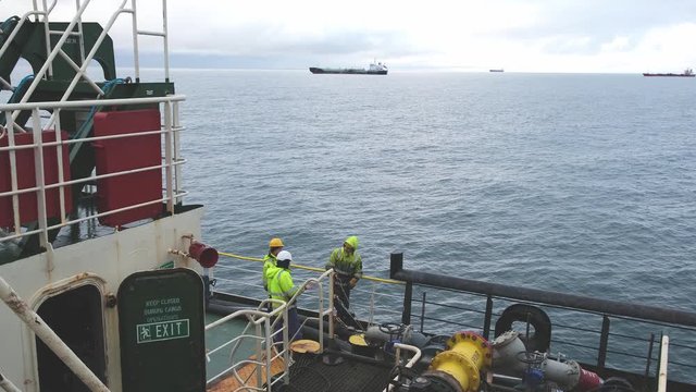 Natig Aliev modern industrial tanker deck crew in yellow reflective vests and helmets stands and chats against sea