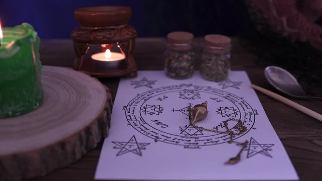 Witchcraft and wizardry. An astrological pendulum for Tarot and an occult circle for divination against a background of burning candles and magical potions. Low light, close-up