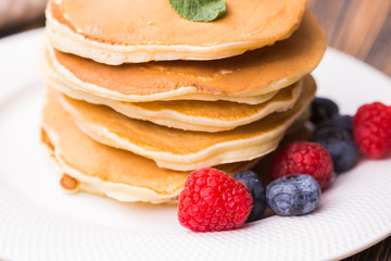 Pile of pancakes with blueberries and raspberries for breakfast on wooden table.