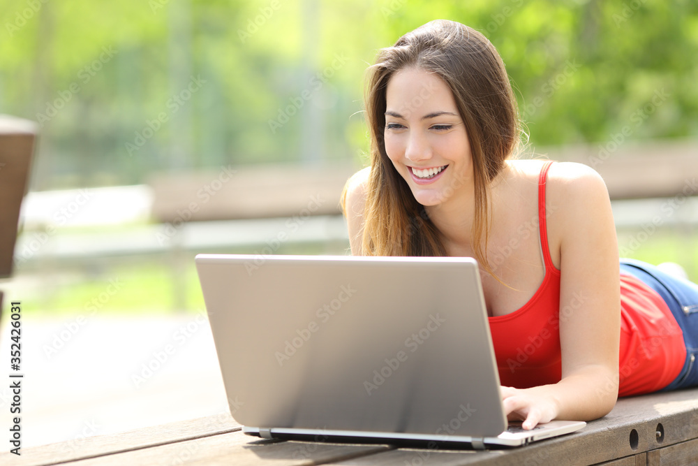 Wall mural happy woman with laptop lying on a park bench