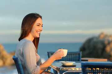 Happy woman contemplating in a coffee shop on the beach