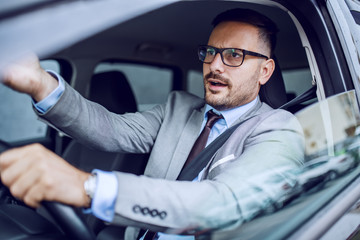 Nervous handsome caucasian businessman in suit and with eyeglasses commenting traffic while sitting...