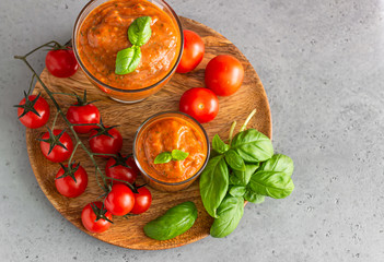Summer homemade cold tomato cream soup in glass. Traditional Spanish soup gazpacho with basil. Grey concrete background.