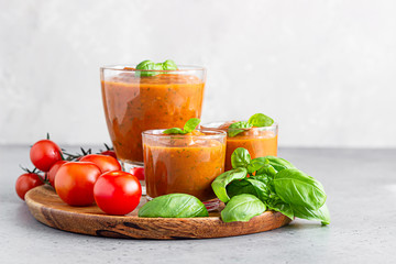 Summer homemade cold tomato cream soup in glass. Traditional Spanish soup gazpacho with basil. Grey concrete background.