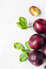 Ripe juicy purple plums, whole and slices, with leaves. Light grey stone background. Healthy vegetarian food. Top view.
