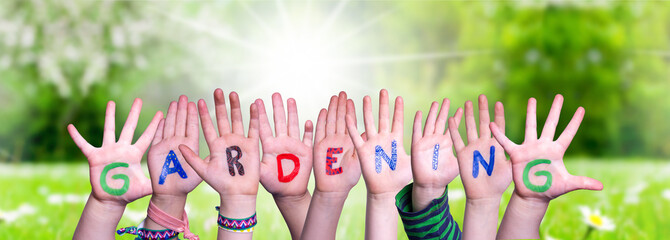 Children Hands Building Colorful English Word Gardening. Sunny Green Grass Meadow As Background