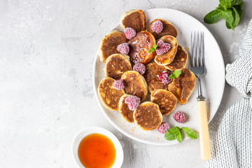 Mini pancakes with raspberries, mint and jam for breakfast on a ceramic plate. Pancakes cooked for breakfast in the home kitchen.