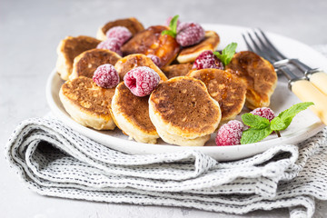 Mini pancakes with raspberries, mint and jam for breakfast on a ceramic plate. Pancakes cooked for breakfast in the home kitchen.