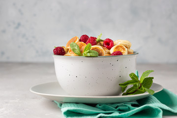 Bowl with tiny pancake cereal with raspberries, mint and jam on a light grey concrete background. Trendy food. Pancake porridge.