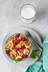 Pancakes cereal with raspberries, mint and jam in a bowl and a glass of milk. Trendy food, tiny funny crumpet, children's food. Breakfast. Top view.