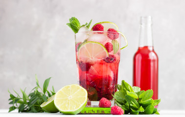 Cold pink non-alcohol cocktail with raspberry, lime, mint and ice cubes on light grey background.