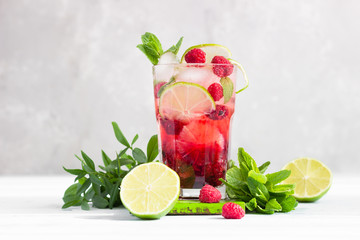 Lemonade or non-alcohol cocktail with raspberry, lime and mint in glass on grey background. Summer...