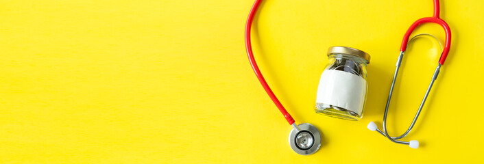 Banner of Savings and insurance concepts. Coins in a bottle with doctor headphones or red stethoscope. Saving for life insurance,retirement,health on the yellow background copy space.