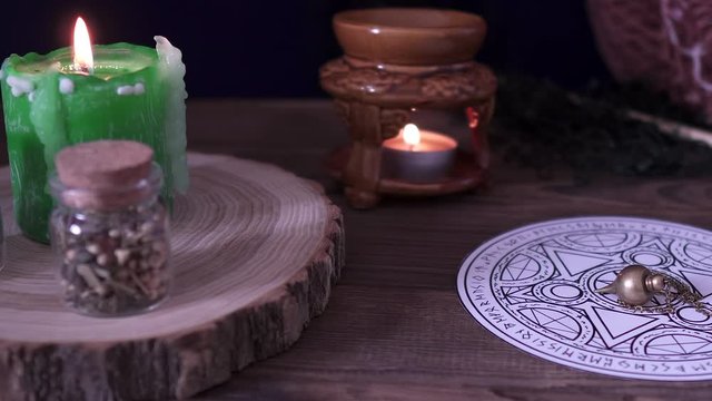 Witchcraft and wizardry. An astrological pendulum for Tarot and an occult circle for divination next to burning green candle, magical potions and subjects. Low light, close-up