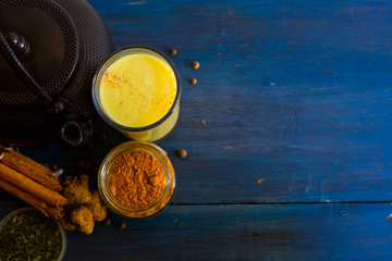 Golden milk powder and a glass with golden milk, on a blue table.