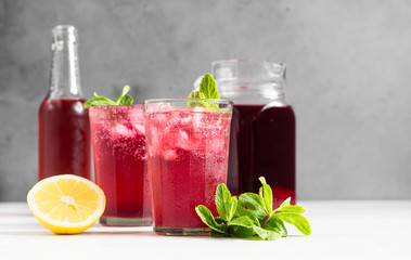 Sparkling pink lemonade with lemon and mint on light grey concrete background.